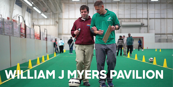 Person escorting blind person on indoor soccer field